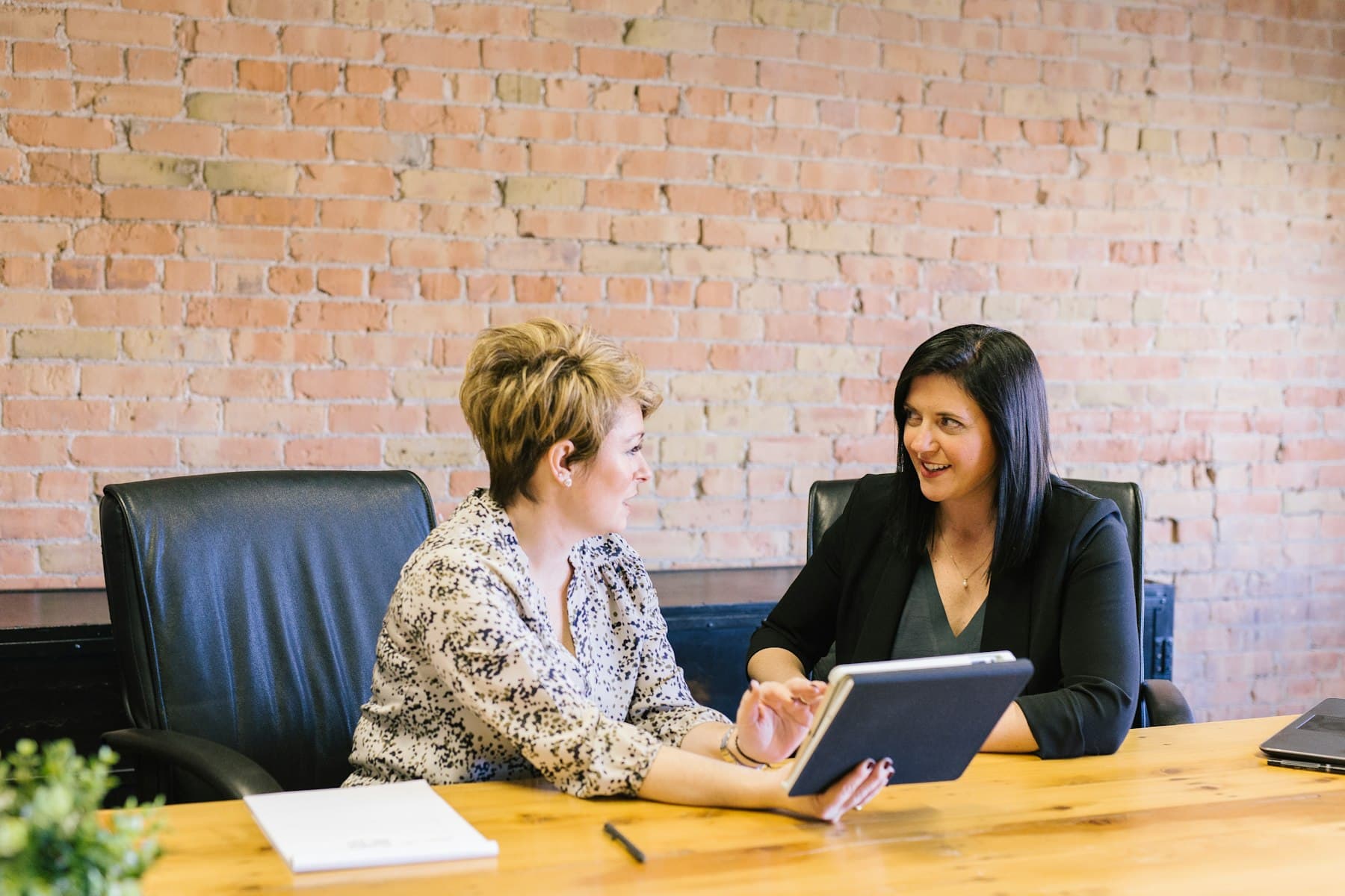 Two women sitting at a table looking at a tablet together, mid-discussion